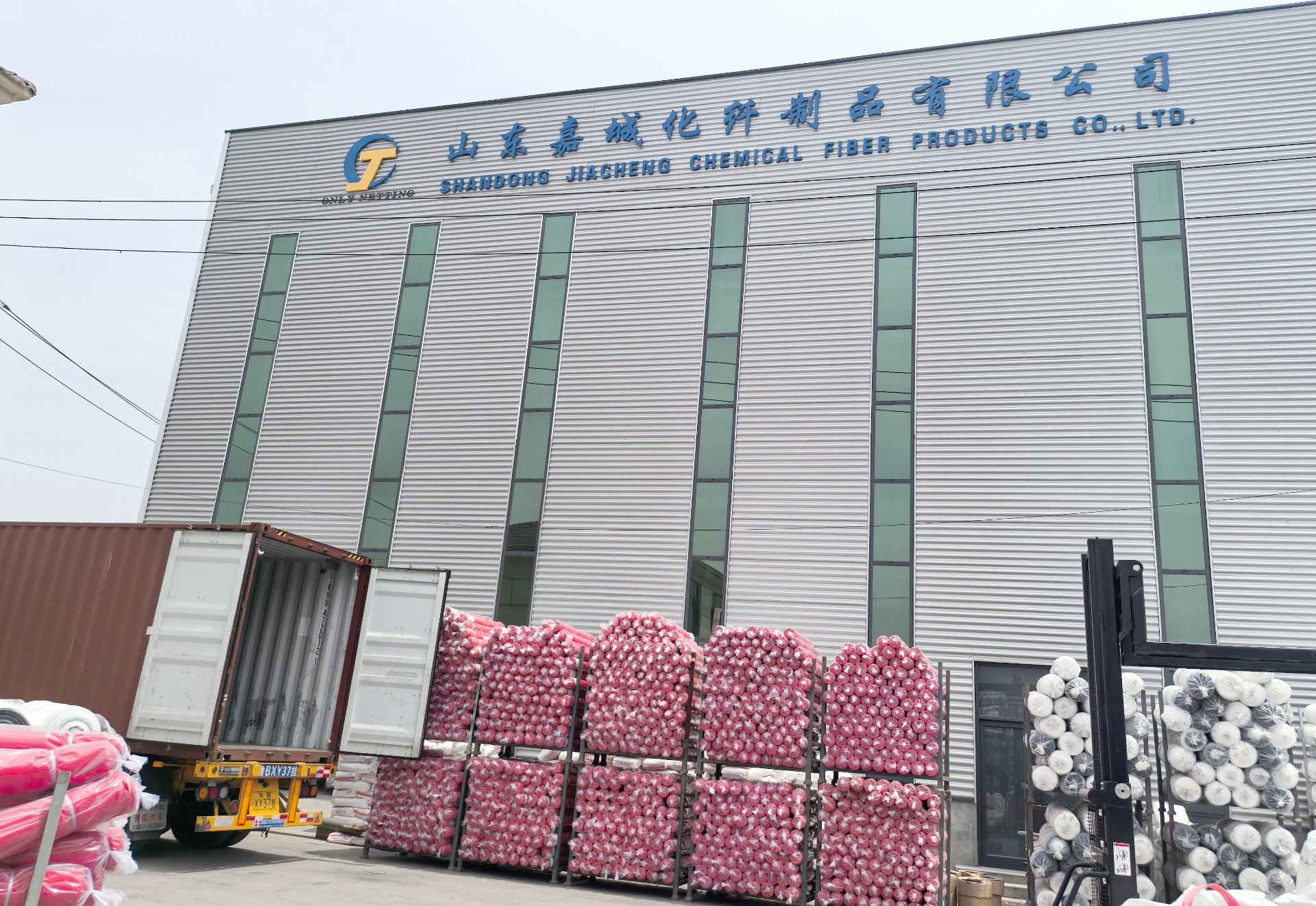 Exterior view of Shandong Jiacheng Chemical Fiber Products Co., Ltd. facility, a leading HDPE netting manufacturer in China, showing a shipping container truck being loaded with finished netting rolls ready for bulk export and direct factory supply
